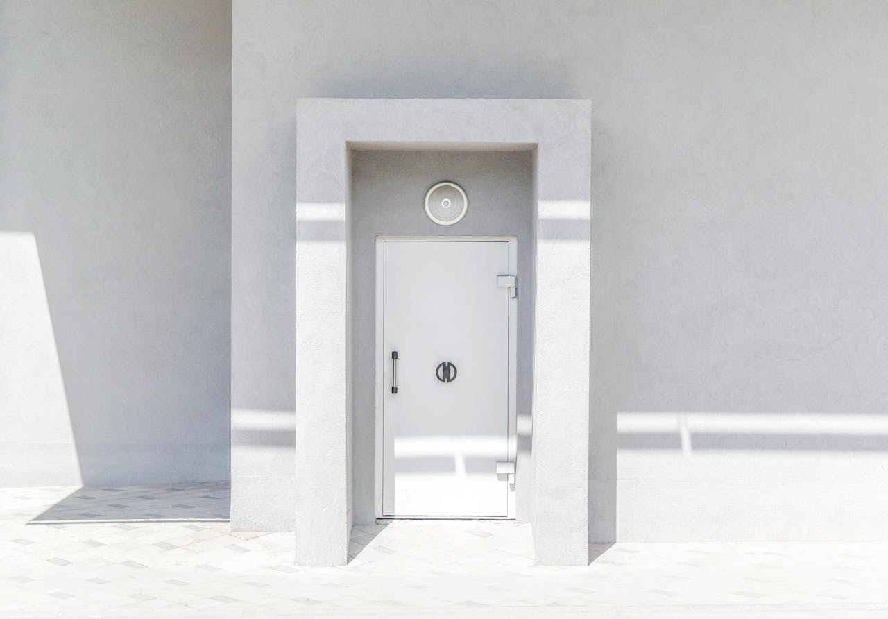 A minimalist white door set against a plain wall, casting geometric shadows in natural sunlight.